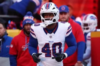 Von Miller in einem weißen Buffalo-Bills-Trikot mit der Nummer 40, mit Helm und Handschuhen, steht auf dem Spielfeld. Inmitten von Gerüchten über Tauschgeschäfte wie "Von Miller wechselt zu den Commanders" erscheinen Teamkollegen und Trainer in Bills-Kleidung im verschwommenen Hintergrund. Diese Beschreibung wurde mit der FootballR KI automatisch generiert.