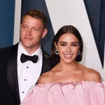 Christian McCaffrey in einem schwarzen Smoking mit Fliege steht lächelnd neben Olivia Culpo in einem schulterfreien rosa Kleid. Sie erscheinen auf einer formellen Veranstaltung mit einem stilvollen dunkel-weiß gemusterten Hintergrund hinter ihnen. Diese Beschreibung wurde mit der FootballR KI automatisch generiert.