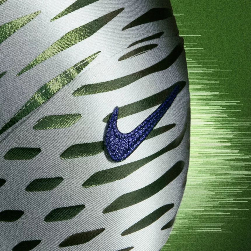 Nahaufnahme eines weißen Sportschuhs mit grünen Schlitzen, einem dunkelblauen Nike-Swoosh-Logo und einem strukturierten grünen Hintergrund, der an NFL Rivalries-Trikots erinnert, mit verschwommenen horizontalen Streifen auf der rechten Seite, die ein Gefühl der Bewegung vermitteln. Diese Beschreibung wurde mit der FootballR KI automatisch generiert.