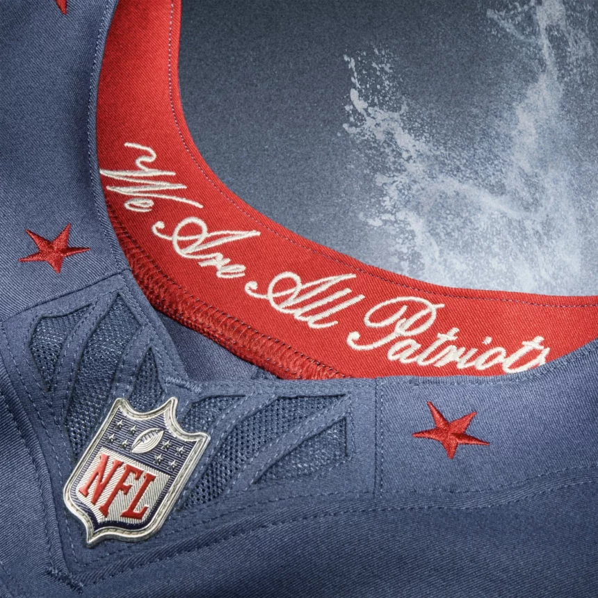 Nahaufnahme eines blauen NFL Rivalries-Trikots mit roter Umrandung am Kragen. Auf dem Kragen steht in weißer Schreibschrift: "We Are All Patriots". Rote Sterne und das NFL-Schildlogo vervollständigen den kultigen Look. Diese Beschreibung wurde mit der FootballR KI automatisch generiert.