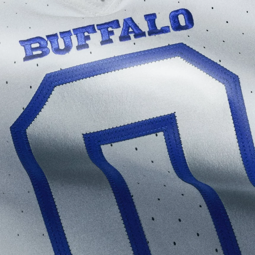 Nahaufnahme eines weißen NFL Rivalries-Trikots mit dem Wort "BUFFALO" in fetten blauen Buchstaben über einer großen blau umrandeten Zahl Null. Kleine Belüftungslöcher sind im Stoff sichtbar. Diese Beschreibung wurde mit der FootballR KI automatisch generiert.