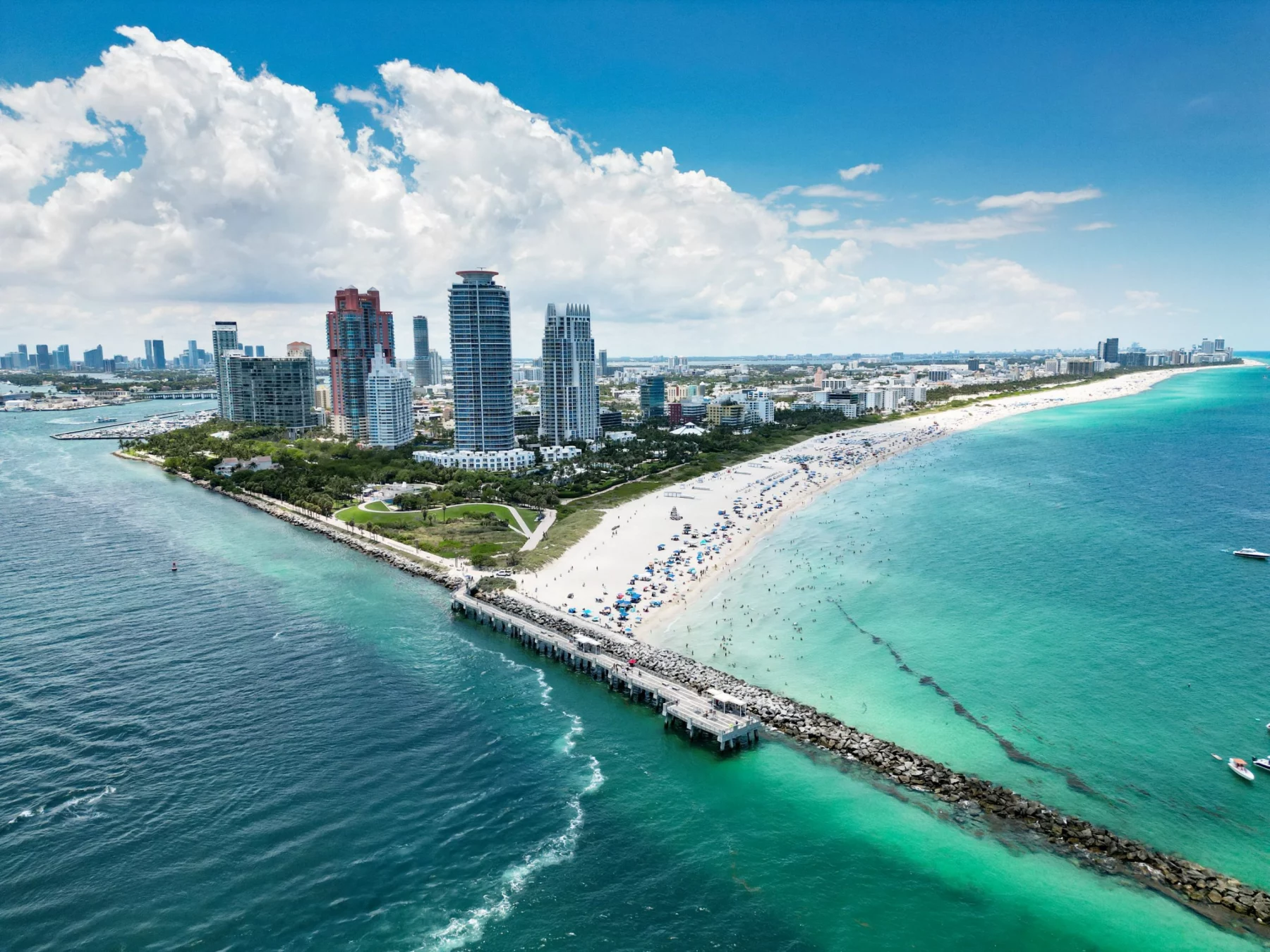 Luftaufnahme einer pulsierenden Stadtlandschaft am Strand mit hohen modernen Gebäuden, wo die Spannung der NFL Preseason entlang des weißen Sandstrandes mit vielen Sonnenanbetern und Sonnenschirmen, türkisfarbenem Meerwasser und einem steinernen Steg unter einem strahlend blauen Himmel zu spüren ist. Diese Beschreibung wurde mit der FootballR KI automatisch generiert.