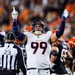 Zach Allen, Footballspieler der Denver Broncos (Nr. 99), jubelt mit erhobenen Armen und nach oben zeigenden Zeigefingern während eines Spiels, umgeben von Teamkollegen und Spielern der Cincinnati Bengals. Ein Schiedsrichter steht in der Nähe, während das Stadionpublikum im Hintergrund verschwommen ist. Diese Beschreibung wurde mit der FootballR KI automatisch generiert.