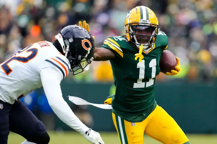 Der Wide Receiver der Green Bay Packers, Jayden Reed, trägt den Football und hält einen Verteidiger der Chicago Bears während eines Spiels fest im Griff. Reed trägt ein grün-gelbes Trikot, während der Spieler der Bears ein weißes Trikot mit marineblauen und orangefarbenen Details trägt. Der Hintergrund ist unscharf. Diese Beschreibung wurde mit der FootballR KI automatisch generiert.