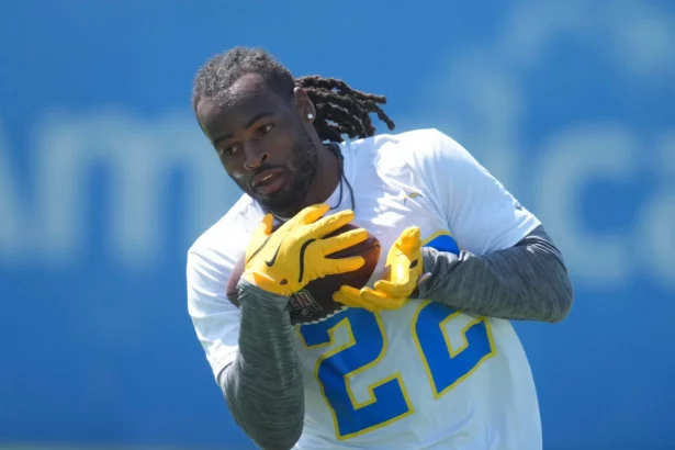 Ein Footballspieler mit Dreadlocks, der Najee Harris ähnelt, trägt ein weißes Trikot mit der Nummer 22 und gelbe Handschuhe und bereitet sich darauf vor, einen Football beim Training zu fangen. Der blaue, leicht verschwommene Hintergrund hebt die Aktion des Sportlers hervor. Diese Beschreibung wurde mit der FootballR KI automatisch generiert.