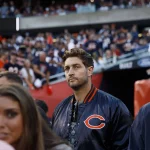 Jay Cutler in einer Jacke der Chicago Bears steht auf dem Football-Feld und blickt direkt in die Kamera, während hinter ihm Massen von Fans - einige mit Jay-Cutler-Trikots - das lebhafte Stadion füllen. Die Szene sprüht vor Energie und Bears-Stolz. Diese Beschreibung wurde mit der FootballR KI automatisch generiert.