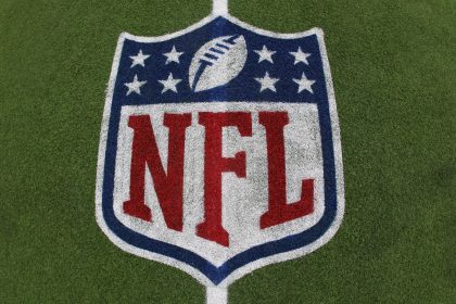 Das NFL-Logo mit dem Football und acht weißen Sternen über dem fetten roten Schriftzug "NFL" ist auf grünem Kunstrasen aufgemalt - ein Symbol, das im Mittelpunkt von Kaderbau und Cap Space Strategien steht, wenn Teams ihren Cap Space für den Erfolg in der Meisterschaft verwalten. Diese Beschreibung wurde mit der FootballR KI automatisch generiert.
