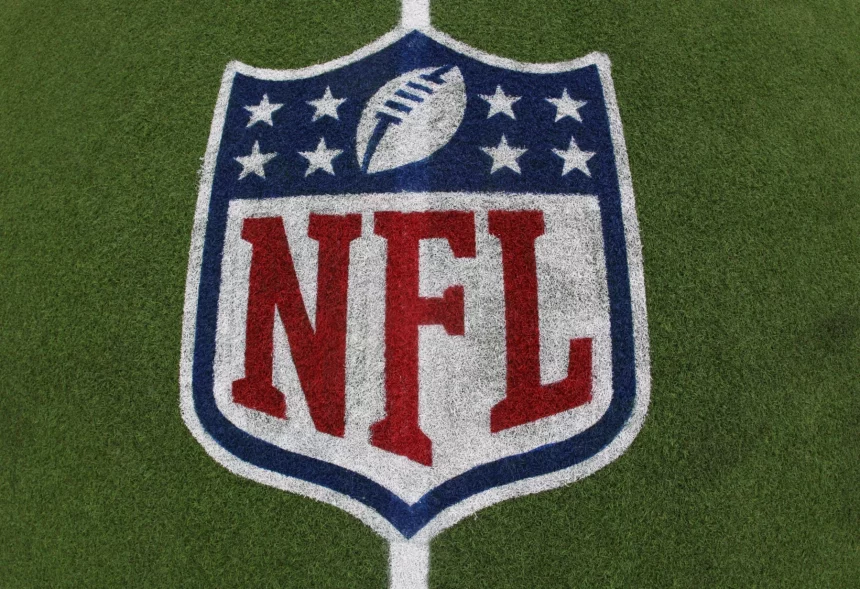 Das NFL-Logo mit dem Football und acht weißen Sternen über dem fetten roten Schriftzug "NFL" ist auf grünem Kunstrasen aufgemalt - ein Symbol, das im Mittelpunkt von Kaderbau und Cap Space Strategien steht, wenn Teams ihren Cap Space für den Erfolg in der Meisterschaft verwalten. Diese Beschreibung wurde mit der FootballR KI automatisch generiert.