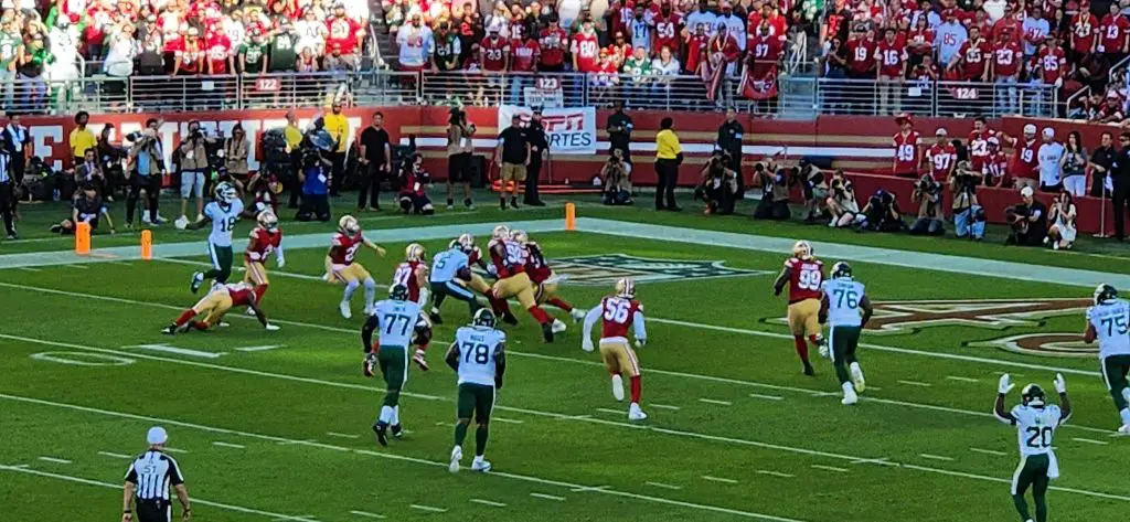 Ein spannendes Footballspiel zwischen den San Francisco 49ers und den New York Jets spielt sich an der Seitenlinie ab, während die Verteidigung der 49ers versucht, ein mögliches Comeback zu verhindern. Die Menge schaut gespannt zu, während die Stars 2025 in Rot, Gold, Weiß und Grün gegeneinander antreten. Diese Beschreibung wurde mit der FootballR KI automatisch generiert.