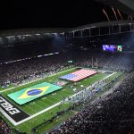 Rio de Janeiro - Ein volles Football-Stadion bei Nacht, in dem ein Spiel der NFL International Series stattfindet, mit großen brasilianischen und amerikanischen Flaggen auf dem Spielfeld. Feuerwerkskörper erhellen den Himmel, während "EAGLES" die Endzone markiert, und Zuschauer aus Brasilien füllen die beleuchteten Tribünen. Diese Beschreibung wurde mit der FootballR KI automatisch generiert.