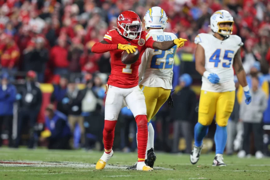 Ein Football-Spieler der Kansas City Chiefs in einer roten Uniform zeigt auf einen Football und feiert auf dem Spielfeld. Xavier Worthy, in einem weiß-gelben Chargers-Trikot mit der Nummer 25, steht in der Nähe, während ein anderer Chargers-Spieler und Fans im Hintergrund jubeln. Diese Beschreibung wurde mit der FootballR KI automatisch generiert.