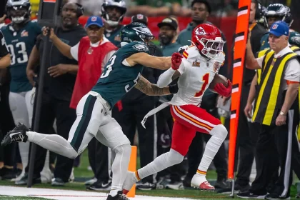 Der Kansas City Chiefs-Spieler Xavier Worthy in einem weiß-roten Trikot läuft mit dem Football, während ein Spieler der Philadelphia Eagles in Grün versucht, ihn zu stoppen. Das Personal an der Seitenlinie und die Schiedsrichter beobachten das Geschehen auf dem Footballfeld. Diese Beschreibung wurde mit der FootballR KI automatisch generiert.
