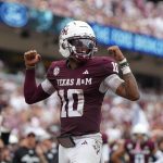 Ein Texas A&M-Football-Spieler, der eine kastanienbraune Uniform mit der Nummer 10, einen weißen Helm und ein Visier trägt, reckt während eines spannenden College Football Spiels in Week 2 jubelnd beide Arme über das Spielfeld. Der unscharfe Hintergrund zeigt eine Menge von Fans auf den Sitzen im Stadion. Diese Beschreibung wurde mit der FootballR KI automatisch generiert.