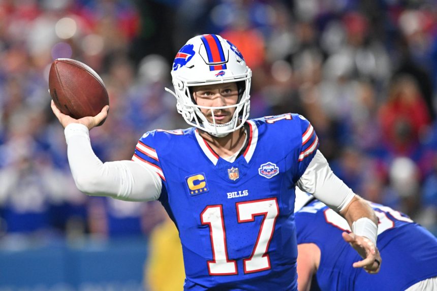 Josh Allen, der seine blaue Bills-Uniform mit der Nummer 17 trägt, bereitet sich darauf vor, während eines Spiels einen Pass zu werfen. Er trägt einen weißen Helm mit dem rot-blauen Buffalo-Logo, während im Hintergrund unscharfe Teamkollegen und das Stadionpublikum zu sehen sind. Diese Beschreibung wurde mit der FootballR KI automatisch generiert.