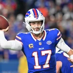 Woche 8 - Free-TV ab 18 Uhr - Josh Allen, der seine blaue Bills-Uniform mit der Nummer 17 trägt, bereitet sich darauf vor, während eines Spiels einen Pass zu werfen. Er trägt einen weißen Helm mit dem rot-blauen Buffalo-Logo, während im Hintergrund unscharfe Teamkollegen und das Stadionpublikum zu sehen sind. Diese Beschreibung wurde mit der FootballR KI automatisch generiert.