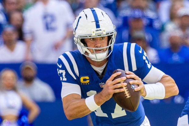 Daniel Jones in einer blauen Uniform der Indianapolis Colts und mit weißem Helm bereitet sich darauf vor, während der NFL Week 1 einen Football zu werfen. Er ist konzentriert und hält den Ball mit beiden Händen, die Nummer 17 ist zwischen Fans und Teamkameraden im Stadionhintergrund zu sehen. Diese Beschreibung wurde mit der FootballR KI automatisch generiert.