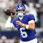 Jaxson Dart übernimmt für Russell Wilson - Ein Footballspieler in einem blauen Trikot mit der Nummer 6 und einem blauen Helm, der Russell Wilson ähnelt, bereitet sich darauf vor, einen Football zu werfen. Er steht während eines Spiels auf dem Feld, den rechten Arm nach hinten gestreckt, mit unscharfen Zuschauern im Hintergrund. Diese Beschreibung wurde mit der FootballR KI automatisch generiert.