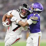 Der Running Back der Atlanta Falcons, Bijan Robinson, versucht sich zu befreien, als ihn ein Verteidiger der Minnesota Vikings in einem lila Trikot bei einem Tackling-Versuch auf einem gut beleuchteten Football-Feld umschließt. Diese Beschreibung wurde mit der FootballR KI automatisch generiert.