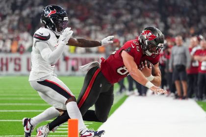 Ein Footballspieler in einem roten Trikot der Tampa Bay Buccaneers springt mit dem Ball in Richtung Endzone, dicht verfolgt von C.J. Gardner-Johnson. Die Aktion findet in der Nähe der Seitenlinie statt, wobei der orangefarbene Pylon die Torlinie markiert. Diese Beschreibung wurde mit der FootballR KI automatisch generiert.