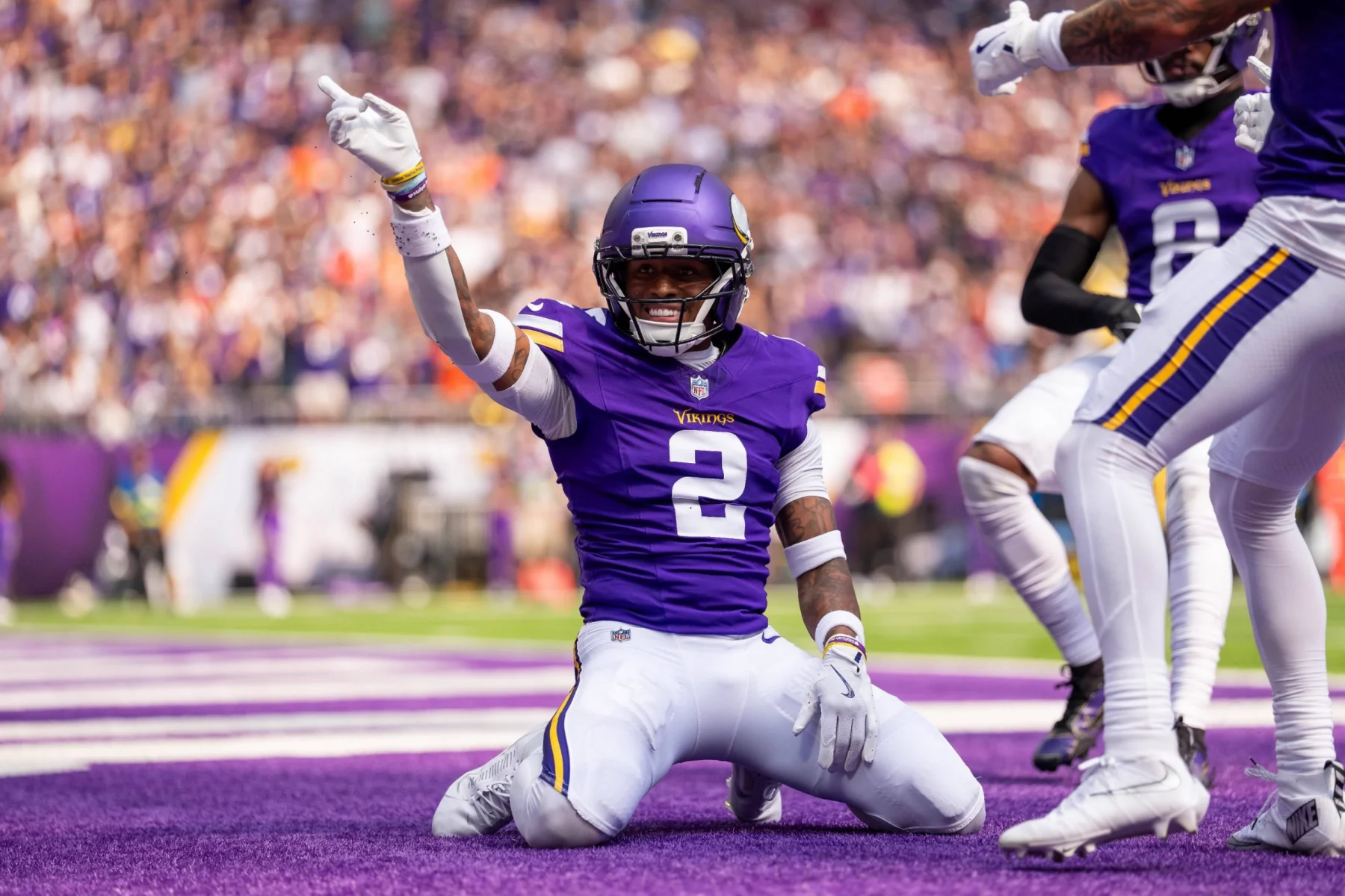 Isaiah Rodgers der Minnesota Vikings in einem lila Trikot mit der Nummer 2 feiert in der NFL WEEK 3 in der Endzone auf den Knien mit erhobenem Arm, umringt von seinen Mannschaftskameraden. Die Menge im Stadion ist im Hintergrund verschwommen. Diese Beschreibung wurde mit der FootballR KI automatisch generiert.