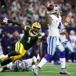 Ein Quarterback der Dallas Cowboys in Weiß und Blau bereitet sich auf den Wurf vor, während ein Verteidiger der Packers in Grün und Gelb auf ihn zustürzt. Andere Spieler und die Zuschauer füllen das Stadion bei diesem spannenden Spiel zwischen Dallas und den Packers. Diese Beschreibung wurde mit der FootballR KI automatisch generiert.