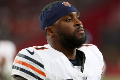 Jaylon Johnson, der eine Chicago Bears-Uniform mit marineblauen und orangefarbenen Streifen und einem passenden Stirnband trägt, steht konzentriert auf dem Spielfeld. Er hat einen kurzen Bart und blickt in die Ferne, wobei der unscharfe Stadionhintergrund seine Präsenz hervorhebt. Diese Beschreibung wurde mit der FootballR KI automatisch generiert.