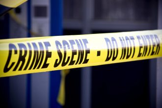 Nahaufnahme von leuchtend gelbem Tatortband mit der Aufschrift "CRIME SCENE - DO NOT ENTER". Das Klebeband markiert den eingeschränkten Zugang, mit einem unscharfen Gebäude und mehr gelbem Klebeband im Hintergrund, wo Mark Sanchez Berichten zufolge in der Nähe eines Krankenhauses festgenommen wurde. Diese Beschreibung wurde mit der FootballR KI automatisch generiert.
