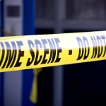 Nahaufnahme von leuchtend gelbem Tatortband mit der Aufschrift "CRIME SCENE - DO NOT ENTER". Das Klebeband markiert den eingeschränkten Zugang, mit einem unscharfen Gebäude und mehr gelbem Klebeband im Hintergrund, wo Mark Sanchez Berichten zufolge in der Nähe eines Krankenhauses festgenommen wurde. Diese Beschreibung wurde mit der FootballR KI automatisch generiert.