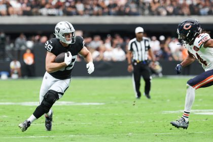 Ein Football-Spieler in einem schwarz-silbernen Raiders-Trikot läuft mit dem Ball und schaut nach vorne, während er von einem Bears-Verteidiger verfolgt wird. Die Aktion ist intensiv, ähnlich wie der herausragende Tight End Brock Bowers, der auf einem leuchtend grünen Feld vor jubelnden Fans spielt. Diese Beschreibung wurde mit der FootballR KI automatisch generiert.