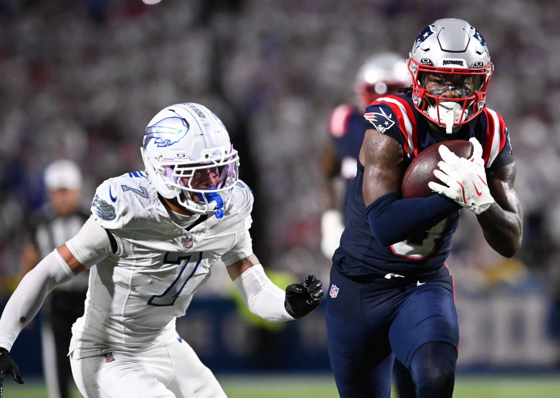 Ein Footballspieler der New England Patriots - Stefon Diggs - in einer Marineuniform läuft mit dem Ball, dicht verfolgt von einem Verteidiger der Buffalo Bills während eines NFL-Spiels. Der unscharfe Hintergrund hebt die Aktion hervor, als die Patriots gegen Stefon Diggs und die Bills antreten. Diese Beschreibung wurde mit der FootballR KI automatisch generiert.