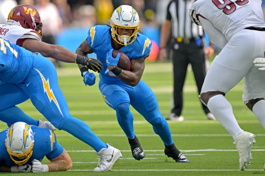 Ein Footballspieler im blauen Trikot der Los Angeles Chargers läuft mit dem Ball und weicht Verteidigern in Weiß und Rot aus. Teamkollegen blockieren, während Runningback Omarion Hampton auf dem grünen Feld nach vorne stürmt, das Gesicht hinter einer gelben Gesichtsmaske. Diese Beschreibung wurde mit der FootballR KI automatisch generiert.
