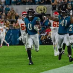 Ein Jacksonville Jaguars Spieler - Devin Lloyd - der Woche rennt mit dem Football in Richtung Endzone, dicht gefolgt von einem Teamkollegen und mehreren Verteidigern der Kansas City Chiefs in diesem spannenden NFL Woche 5 Spiel, während die Menge im Stadion jubelt. Diese Beschreibung wurde mit der FootballR KI automatisch generiert.