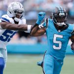 Rico Dowdle - Ein Spieler der Carolina Panthers in Grün (#5) rennt mit dem Football und hält den Cowboys-Verteidiger in Weiß und Blau auf, als dieser ihn tacklen will. Ein Schiedsrichter steht während dieses Moments in der NFL Recap Week 6 unscharf im Hintergrund. Diese Beschreibung wurde mit der FootballR KI automatisch generiert.