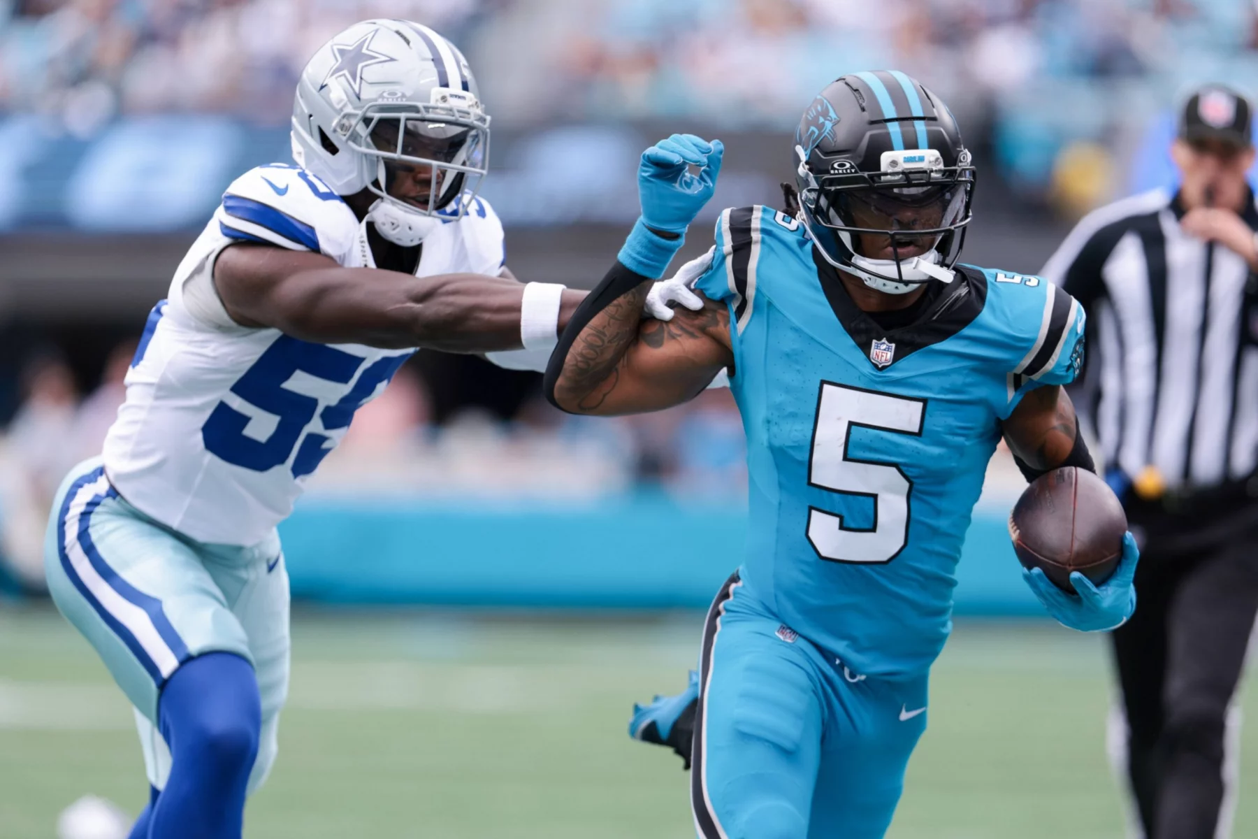 Spieler der Woche Rico Dowdle - Ein Spieler der Carolina Panthers in Grün (#5) rennt mit dem Football und hält den Cowboys-Verteidiger in Weiß und Blau auf, als dieser ihn tacklen will. Ein Schiedsrichter steht während dieses Moments in der NFL Recap Week 6 unscharf im Hintergrund. Diese Beschreibung wurde mit der FootballR KI automatisch generiert.