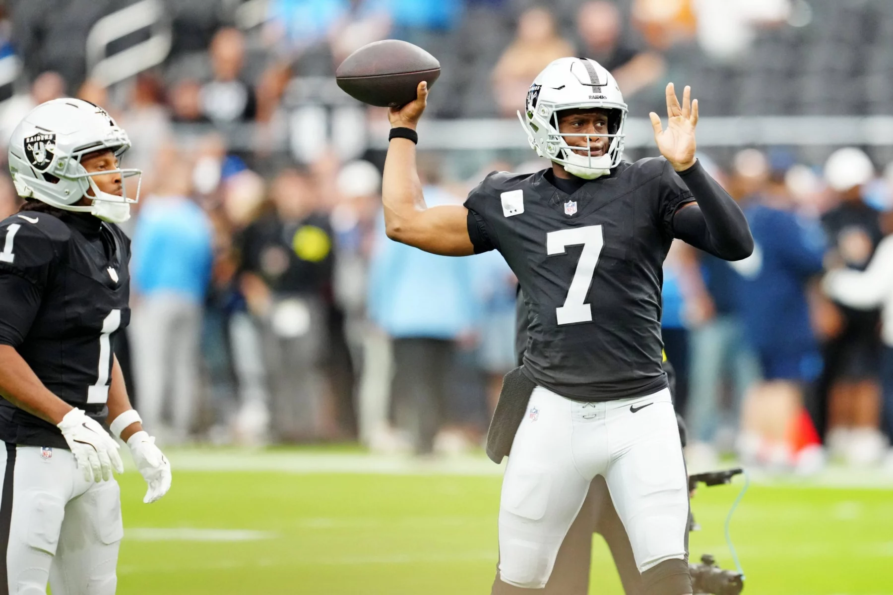 Geno Smith, der in einem schwarzen Trikot mit der Nummer 7 und einem silbernen Helm Quarterback Leistungen zeigt, befindet sich während der Saison 2025 mitten im Wurf. Ein anderer Mannschaftskamerad steht in der Nähe vor einer verschwommenen Menge und einem grünen Feld. Diese Beschreibung wurde mit der FootballR KI automatisch generiert.