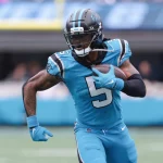 Rico Dowdle in einem blauen Trikot der Carolina Panthers mit der Nummer 5 läuft während eines Spiels mit dem Ball. Chuba Hubbard, einer der dynamischen RBs des Teams, trägt einen Helm und Handschuhe und blickt entschlossen nach vorne. Das Stadion und das Spielfeld verschwimmen im Hintergrund. Diese Beschreibung wurde mit der FootballR KI automatisch generiert.
