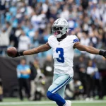 George Pickens, Dallas Cowboys, der die Trikotnummer 3 trägt, feiert mit ausgestreckten Armen, während er einen Football in der Hand hält, umgeben von einer unscharfen Menschenmenge in einem Stadion - vielleicht nach einem großen Spielzug oder einer gerüchteweisen Vertragsverlängerung mit den Cowboys. Diese Beschreibung wurde mit der FootballR KI automatisch generiert.