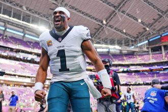 Ein Footballspieler im weißen Trikot der Philadelphia Eagles mit der Nummer 1 ballt die Fäuste und jubelt auf dem Spielfeld während der NFL Woche 7. Das Stadion ist voll mit lila Sitzen und Menschen, während Kameras und Medien diesen elektrisierenden Moment festhalten. Diese Beschreibung wurde mit der FootballR KI automatisch generiert.