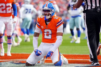 Broncos-Star-Cornerback Pat Surtain II in seinem orangefarbenen Trikot mit der Nummer 2 kniet auf dem Spielfeld, ballt die Fäuste und schreit vor der jubelnden Menge im Stadion, während Spieler in Blau und Weiß und ein Schiedsrichter in der Nähe stehen. Diese Beschreibung wurde mit der FootballR KI automatisch generiert.