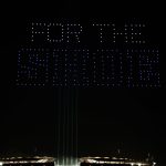 Nachts erhellt eine Drohnenshow den Berliner Himmel, während Drohnen in leuchtendem Blau "FOR THE SHOE" über einem glühenden Stadion buchstabieren. Vier vertikale Balken ragen nach oben und verstärken die dramatische Hommage an die Colts in der umgebenden Dunkelheit. Diese Beschreibung wurde mit der FootballR KI automatisch generiert.