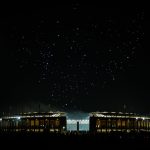 Ein hell erleuchtetes Stadion in Berlin erhebt sich gegen den Nachthimmel, im Vordergrund sind Menschenmengen zu erkennen. Oben bilden Dutzende kleiner glühender Lichter eine Drohnenshow, während auf der linken Seite des Himmels der Vollmond leuchtet. Diese Beschreibung wurde mit der FootballR KI automatisch generiert.