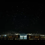 Ein hell erleuchtetes Stadion in Berlin erhebt sich gegen den Nachthimmel, im Vordergrund sind Menschenmengen zu erkennen. Oben bilden Dutzende kleiner glühender Lichter eine Drohnenshow, während auf der linken Seite des Himmels der Vollmond leuchtet. Diese Beschreibung wurde mit der FootballR KI automatisch generiert.