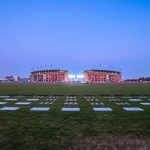 Ein weites, grasbewachsenes Feld führt zu einem großen, mit Fahnen geschmückten Stadion. Der Himmel ist klar und geht in der Nähe des Horizonts von Hellblau in Lila über. Auf dem Spielfeld sind riesige Schachfiguren aufgestellt - vielleicht für eine Veranstaltung zum Thema Colts oder eine Berliner Drohnenshow. Diese Beschreibung wurde mit der FootballR KI automatisch generiert.