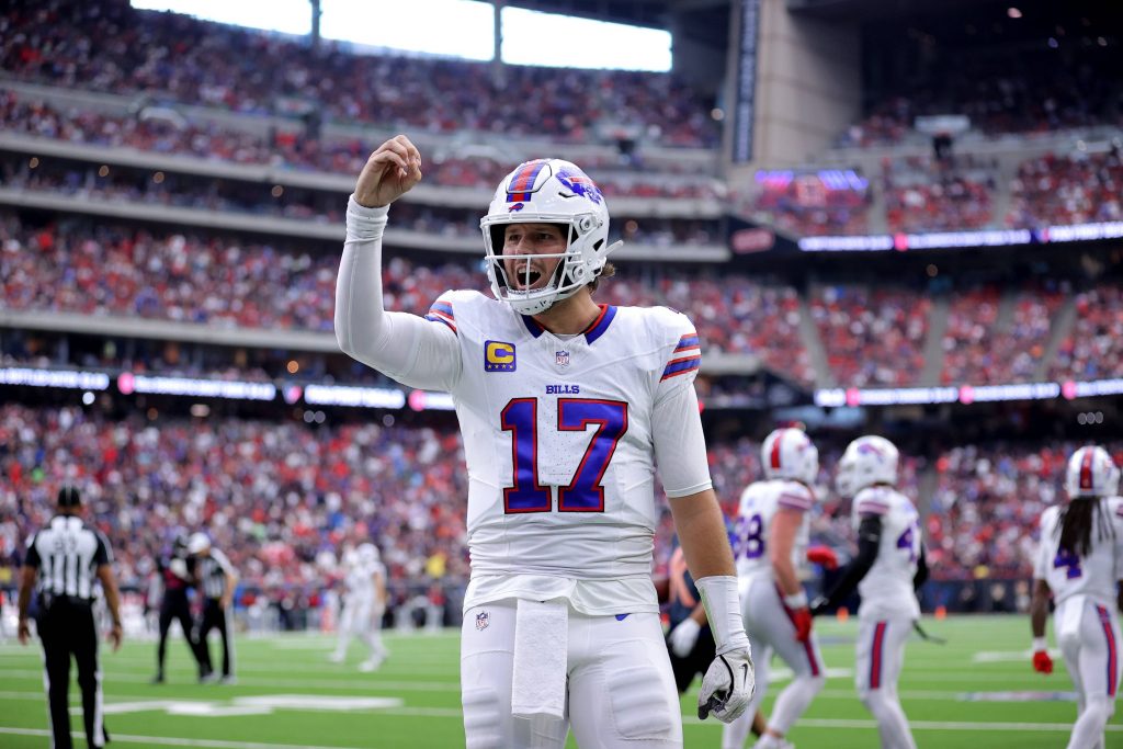 Josh Allen - Woche 11 - Woche 15 - Ein Footballspieler im weißen Trikot der Buffalo Bills mit der Nummer 17 steht mitten im Spiel auf dem Feld und hebt die rechte Hand. In diesem Rückblick tragen das überfüllte Stadion und die Anwesenheit des Spielers der Woche zu einer spannenden Atmosphäre bei. Diese Beschreibung wurde mit der FootballR KI automatisch generiert.