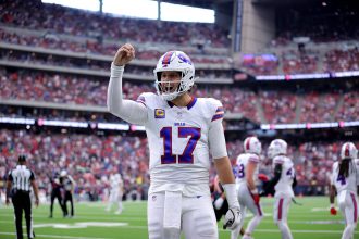 Josh Allen - Woche 11 - Ein Footballspieler im weißen Trikot der Buffalo Bills mit der Nummer 17 steht mitten im Spiel auf dem Feld und hebt die rechte Hand. In diesem Rückblick tragen das überfüllte Stadion und die Anwesenheit des Spielers der Woche zu einer spannenden Atmosphäre bei. Diese Beschreibung wurde mit der FootballR KI automatisch generiert.