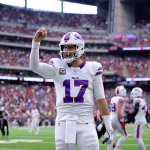 Josh Allen - Woche 11 - Woche 15 - Ein Footballspieler im weißen Trikot der Buffalo Bills mit der Nummer 17 steht mitten im Spiel auf dem Feld und hebt die rechte Hand. In diesem Rückblick tragen das überfüllte Stadion und die Anwesenheit des Spielers der Woche zu einer spannenden Atmosphäre bei. Diese Beschreibung wurde mit der FootballR KI automatisch generiert.