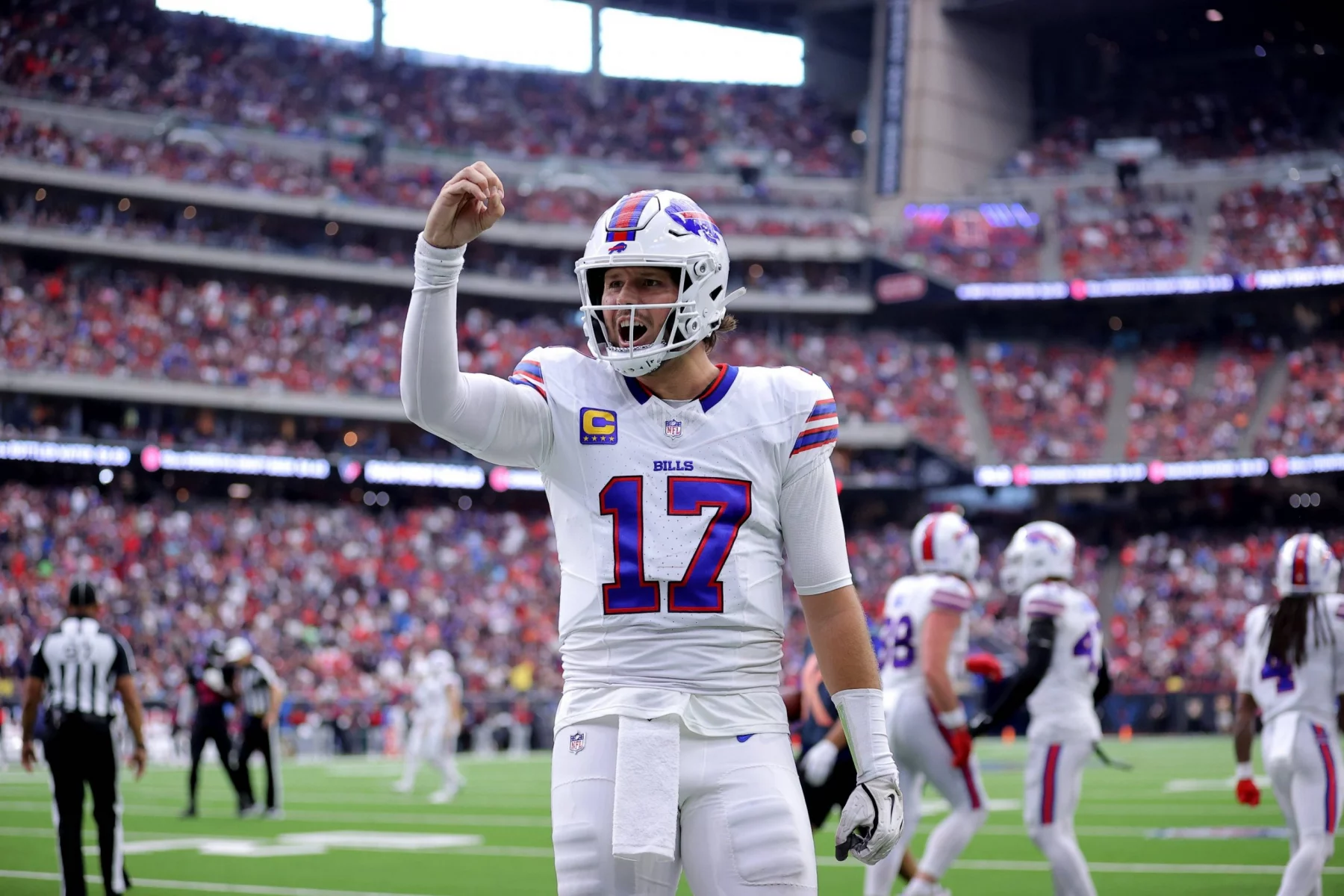 Josh Allen - Woche 11 - Woche 15 - Ein Footballspieler im weißen Trikot der Buffalo Bills mit der Nummer 17 steht mitten im Spiel auf dem Feld und hebt die rechte Hand. In diesem Rückblick tragen das überfüllte Stadion und die Anwesenheit des Spielers der Woche zu einer spannenden Atmosphäre bei. Diese Beschreibung wurde mit der FootballR KI automatisch generiert.