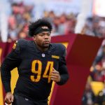 Daron Payne in einer schwarzen Uniform mit der Nummer 94, die einem Commanders Verteidiger ähnelt, läuft auf das Spielfeld. Rauch und eine große "W"-Struktur tauchen im Hintergrund auf, während die konzentrierte Menge seinen entschlossenen Auftritt verfolgt. Diese Beschreibung wurde mit der FootballR KI automatisch generiert.