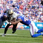 Zwei Verteidiger der Buffalo Bills in blauen Uniformen greifen den Saints-Receiver Brandin Cooks an, der den Football während eines NFL-Spiels in der Hand hält. Die Szene spielt auf einem sonnenbeschienenen Feld mit einer unscharfen Menschenmenge im Stadionhintergrund. Diese Beschreibung wurde mit der FootballR KI automatisch generiert.