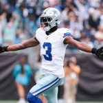 George Pickens der Dallas Cowboys mit der Trikotnummer 3 breitet seine Arme aus, während er einen Football hält und auf dem Spielfeld feiert. Er trägt einen silbernen Helm und eine weiße Uniform, während Cheerleader und Fans im Hintergrund des Cowboys-Stadions verschwimmen. Diese Beschreibung wurde mit der FootballR KI automatisch generiert.